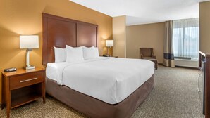 A hotel room with a large bed, bedside tables with lamps, a chair, and a large window with curtains. - Comfort Inn North Conroe (Conroe)
