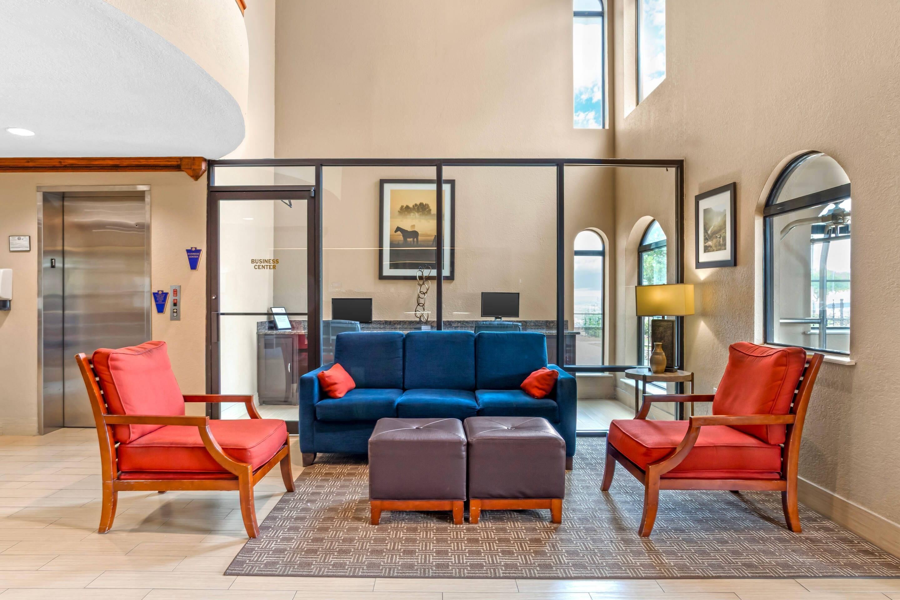 A lobby with a blue sofa, two red chairs, a wooden coffee table, and a patterned rug.