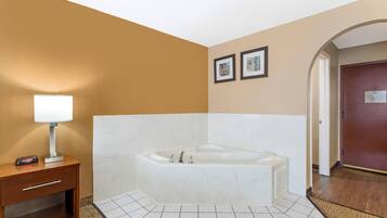 A hotel bathroom with a bathtub, a bedside table with a lamp, and two framed pictures on the wall.