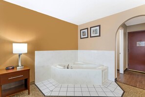 A hotel bathroom with a bathtub, a bedside table with a lamp, and two framed pictures on the wall.