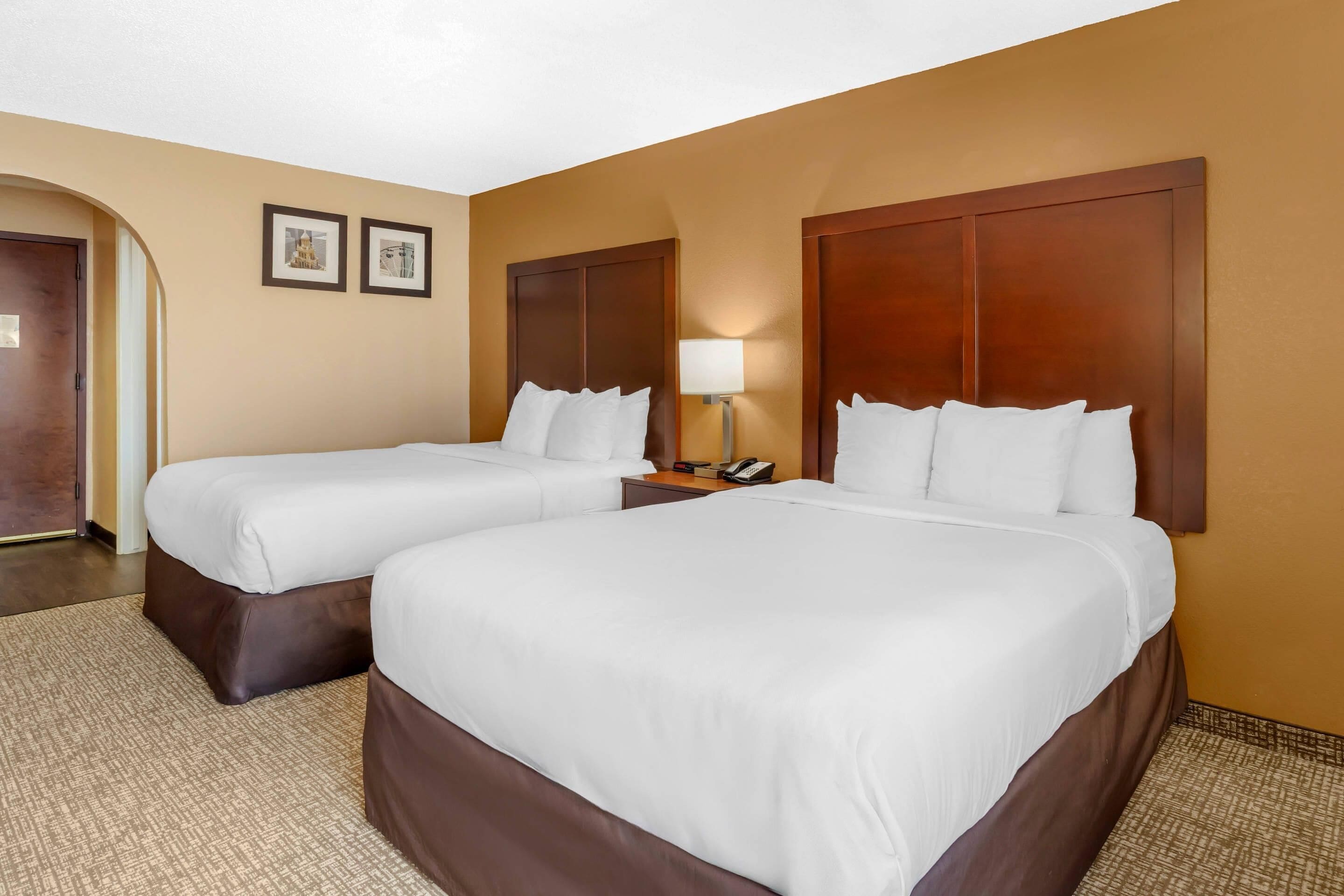 A hotel room with two beds, a nightstand with a lamp, and a door.