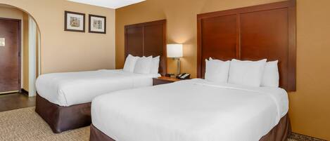 A hotel room with two beds, a nightstand with a lamp, and a door.