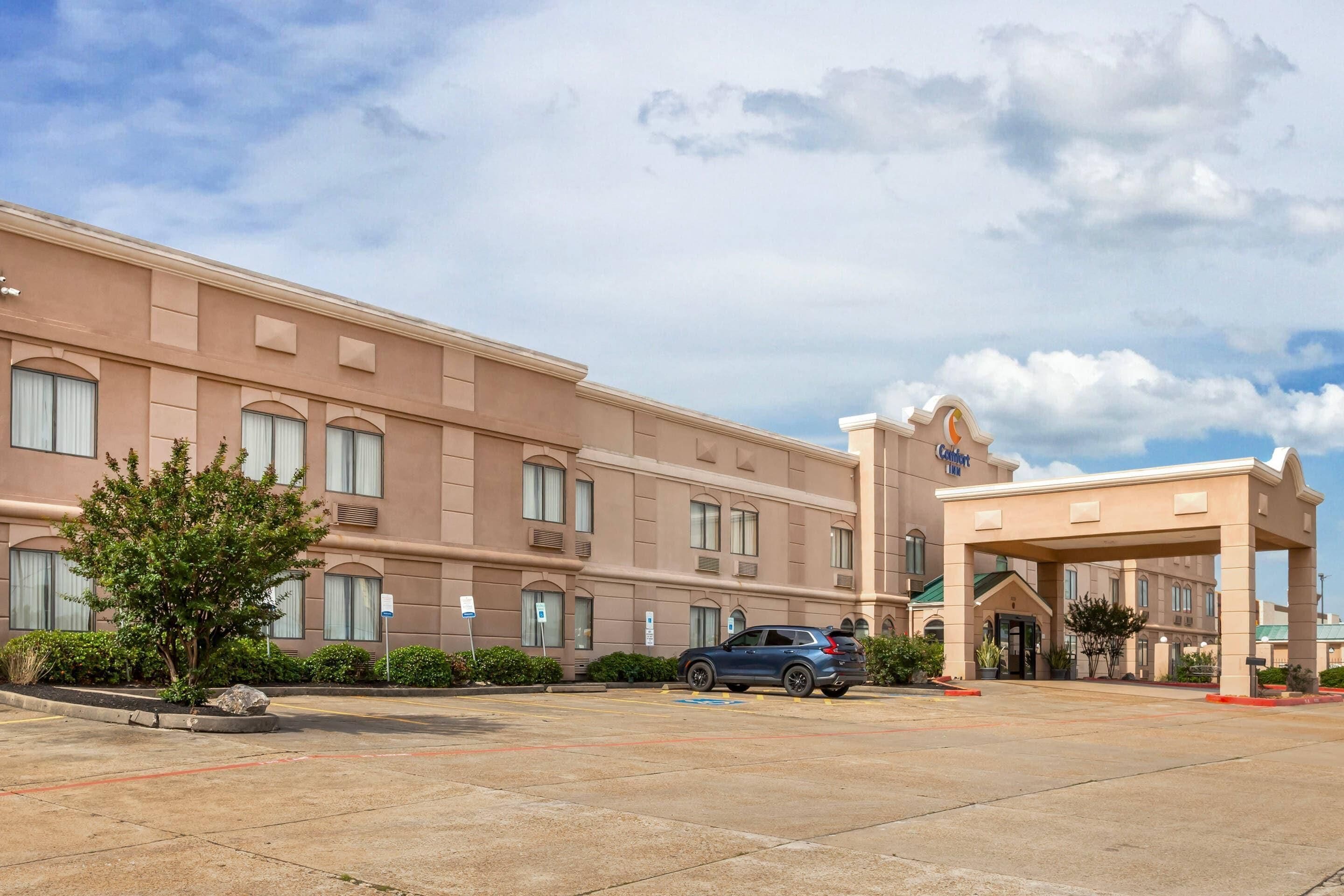 A hotel with a large parking lot, a covered entrance, and a building facade with multiple windows.