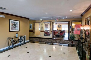 Vestíbulo de hotel con piso de mármol, un mostrador de recepción, una obra de arte enmarcada y un área de comedor visible a través de una puerta abierta.