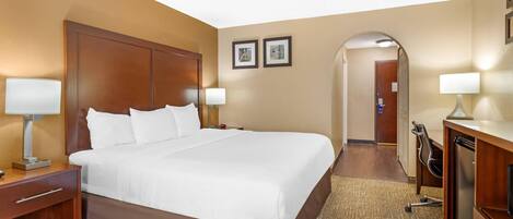 A hotel room with a large bed, two bedside lamps, a wooden headboard, a desk with a lamp, and a desk lamp.