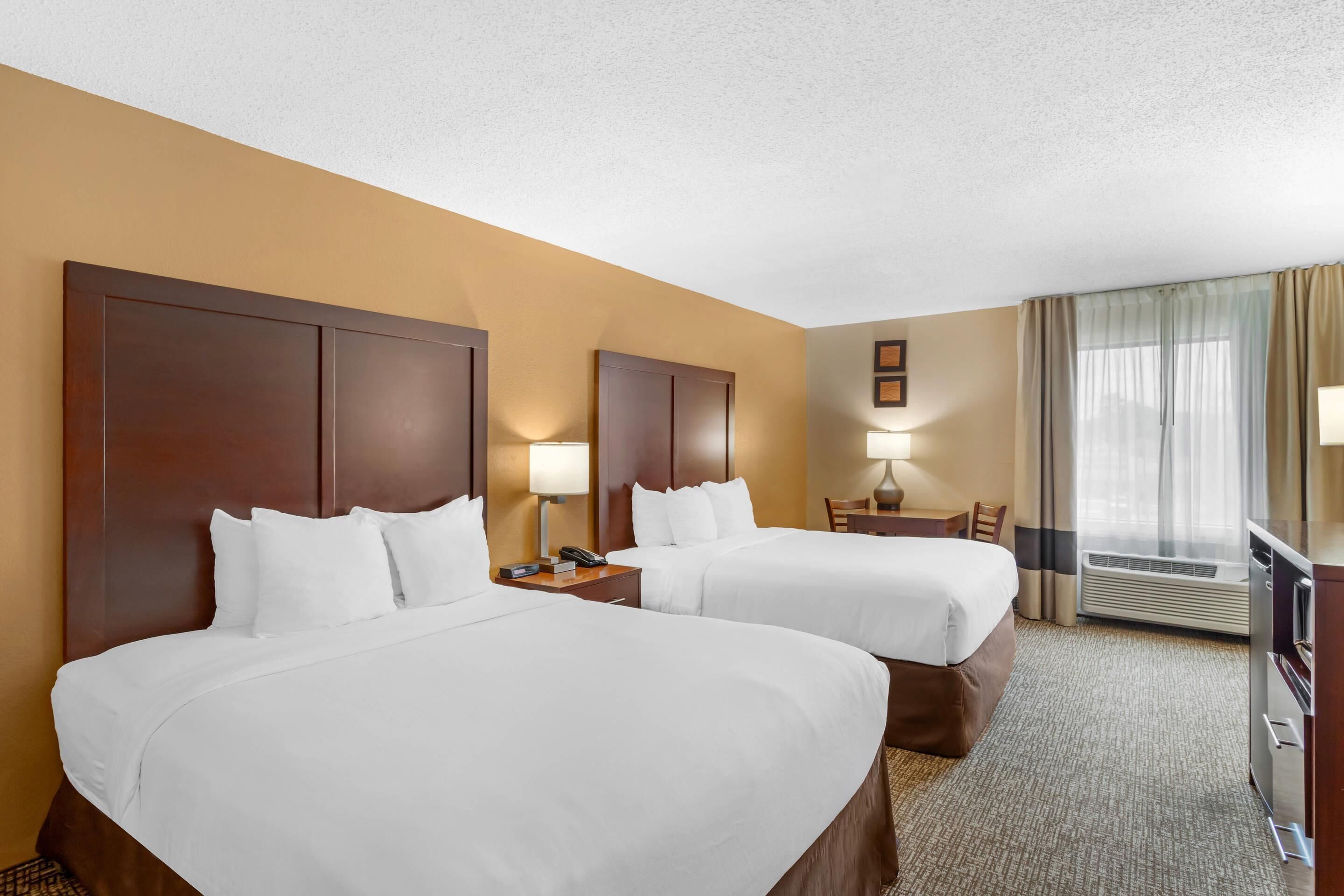 Une chambre d’hôtel avec deux lits, un bureau, une chaise, une lampe et un téléviseur.