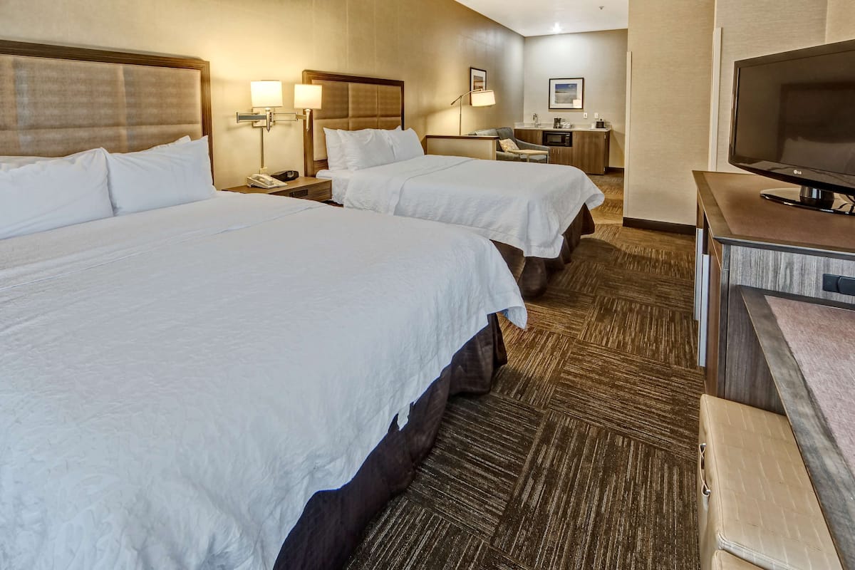 A hotel room with two beds, a desk, a television, and a bathroom.