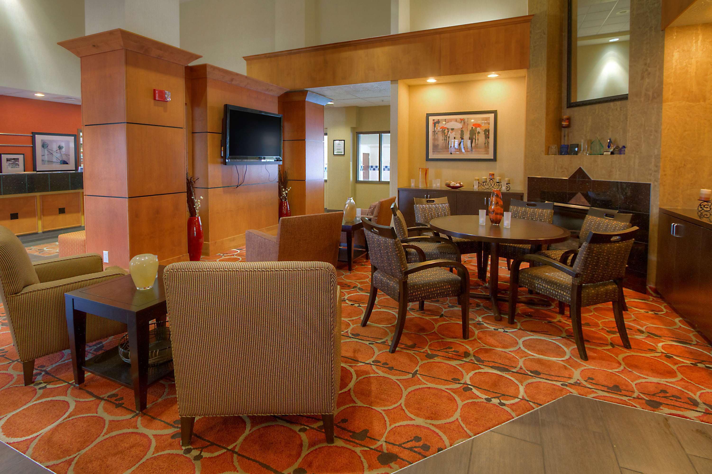 A hotel lobby with a round dining table, several chairs, a television, and a patterned carpet.