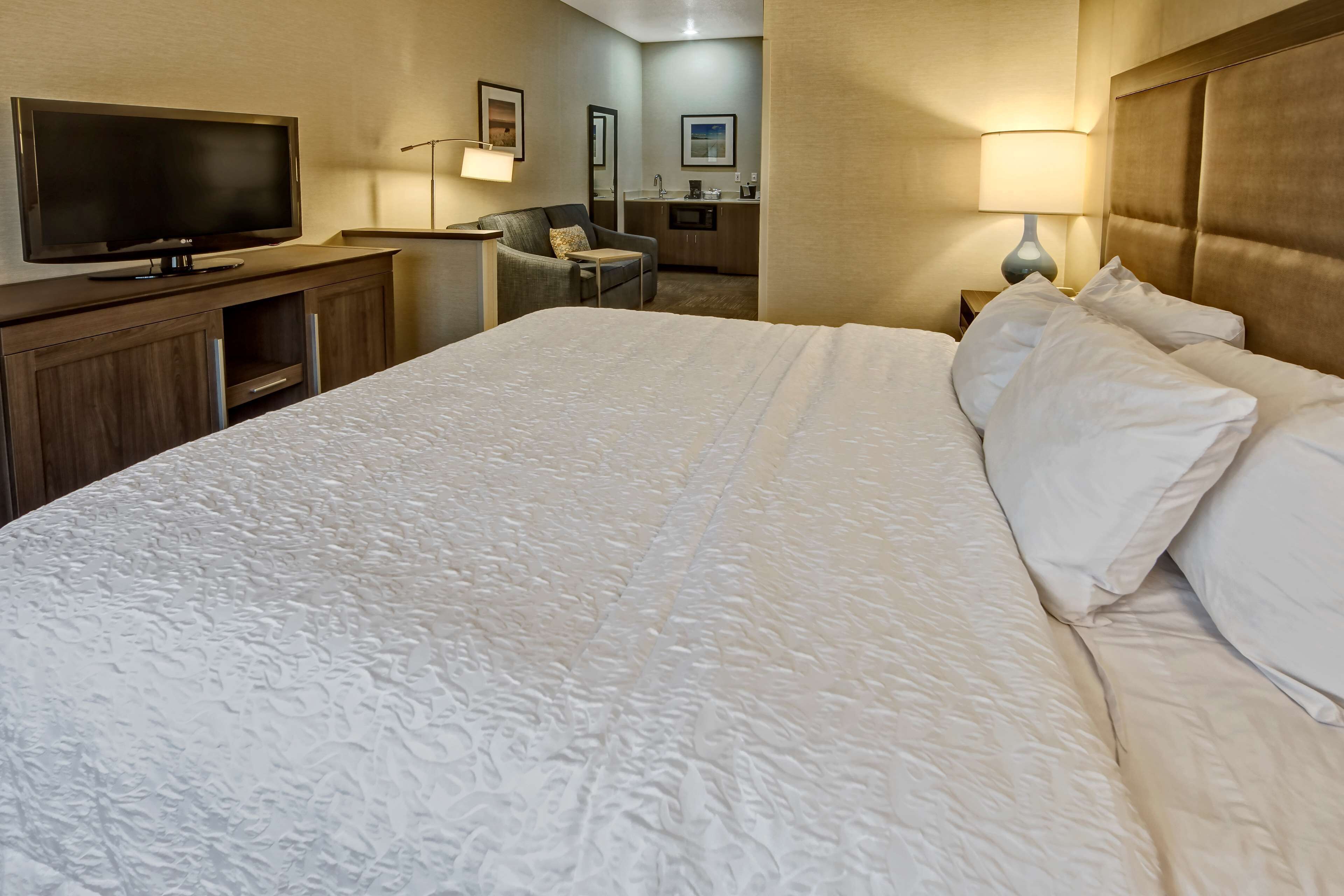 Hotelkamer met een groot bed, een flatscreen televisie, een bureau met stoel, een kitchenette en een zichtbare badkamer op de achtergrond.