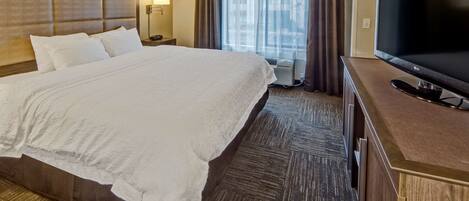 A hotel room with a large bed, a flat-screen TV, a bedside table, and a window with curtains.
