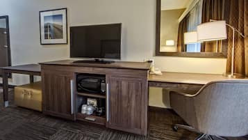 Habitación de hotel con un escritorio de madera, televisor de pantalla plana, lámpara, silla y minibar.