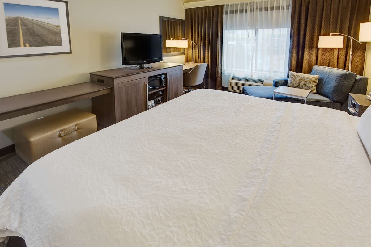 A hotel room with a large bed, a desk with a television, a chair, a small table, and a sofa.