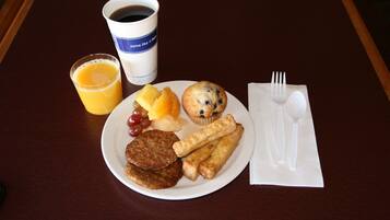 A breakfast plate with pancakes, a muffin, sausage links, and a glass of orange juice on a table.