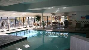 An indoor swimming pool with clear glass walls, a tiled floor, and several seating areas with chairs and tables. - Hampton Inn Salt Lake City/Layton (Layton)