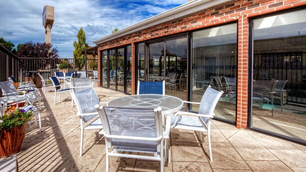 An outdoor patio with round tables and chairs, a brick wall, and large windows. - Hampton Inn Salt Lake City/Layton (Layton)
