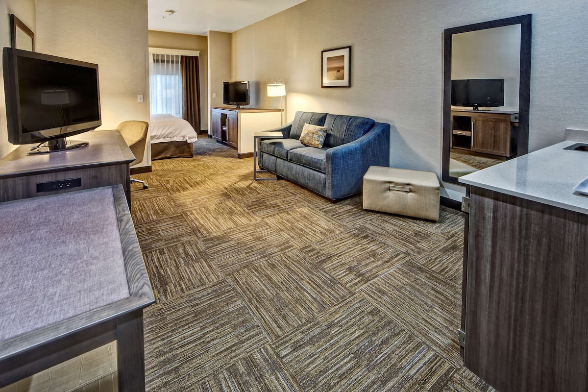 A hotel room with a flat-screen TV, a sofa, a desk, a bed, and a bathroom area.