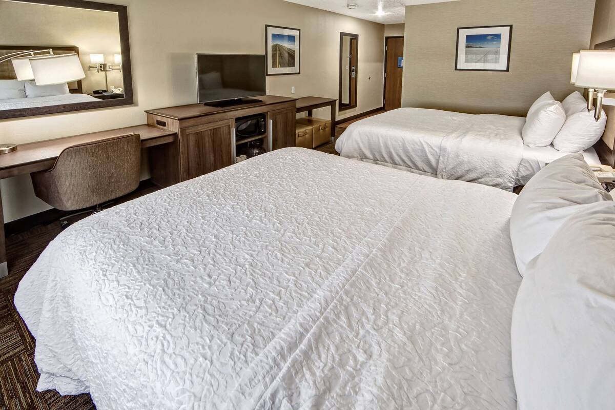 A hotel room with two beds, a desk with a computer, a mirror, and a TV.
