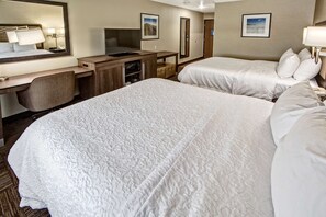 A hotel room with two beds, a desk with a computer, a mirror, and a TV.