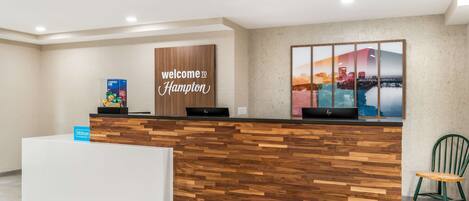 A reception desk with a 'Welcome to Hampton' sign, a cityscape poster, and a 'Hilton' sign.