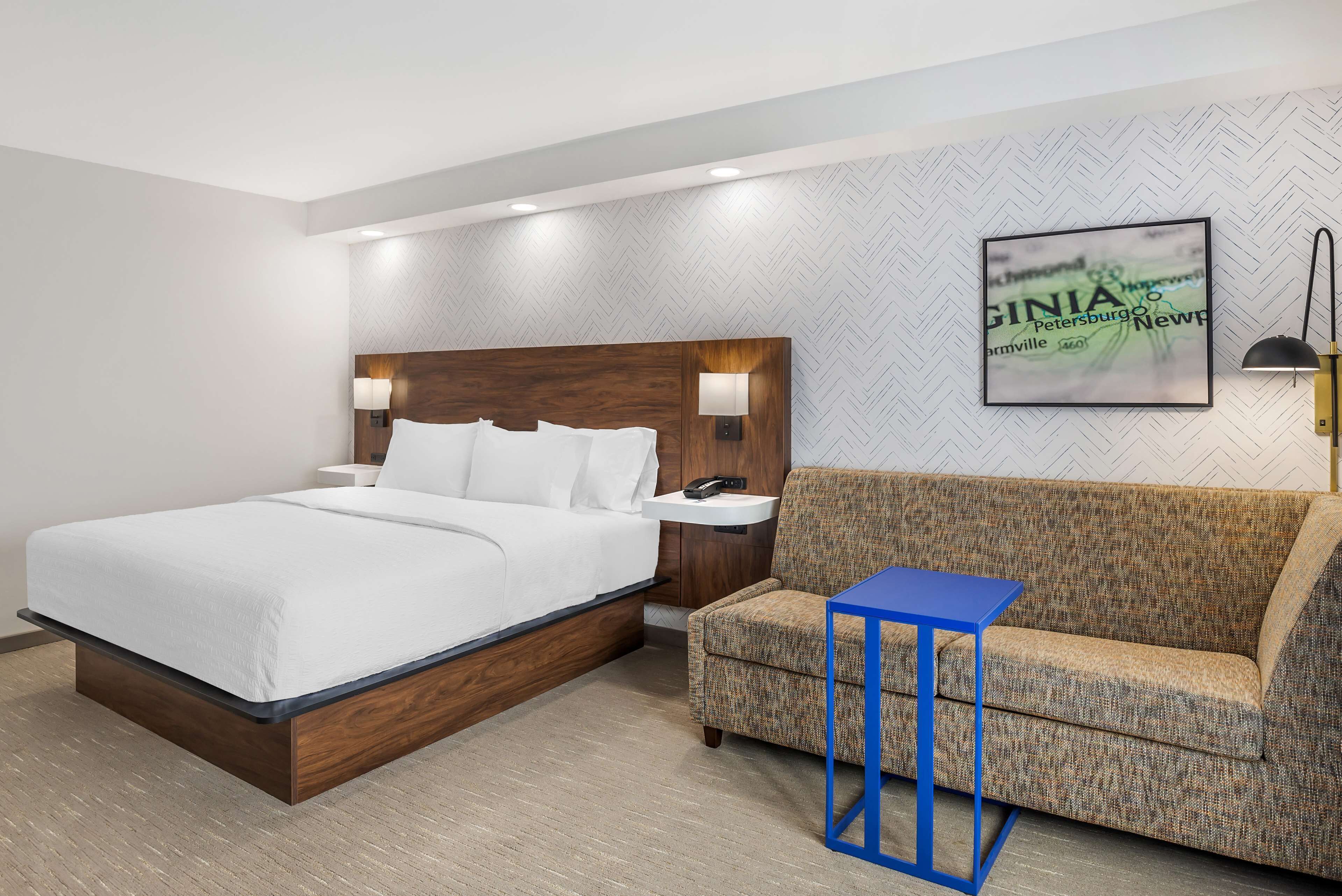 Une chambre d’hôtel avec un grand lit, un canapé, une petite table et une lampe fixée au mur.