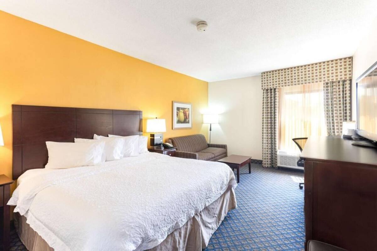 Una habitación de hotel con una cama grande, un escritorio, una silla, un sofá y un televisor.