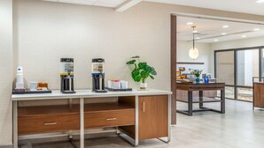 Una habitación de hotel moderna con un escritorio de madera, una cafetera, una planta y un ventanal grande.