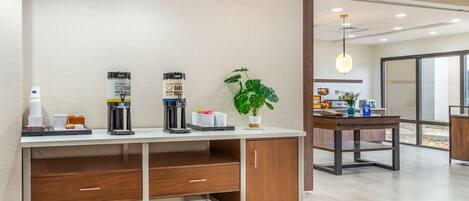 A modern hotel room with a wooden desk, a coffee machine, a plant, and a large window.