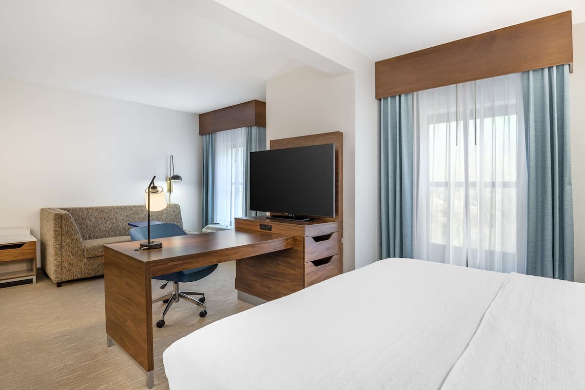 Habitación de hotel con una cama grande, un escritorio de madera, un televisor de pantalla plana, un sofá y una lámpara.