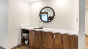 Un baño moderno con una encimera blanca, un espejo redondo, un lavabo y armarios de madera.
