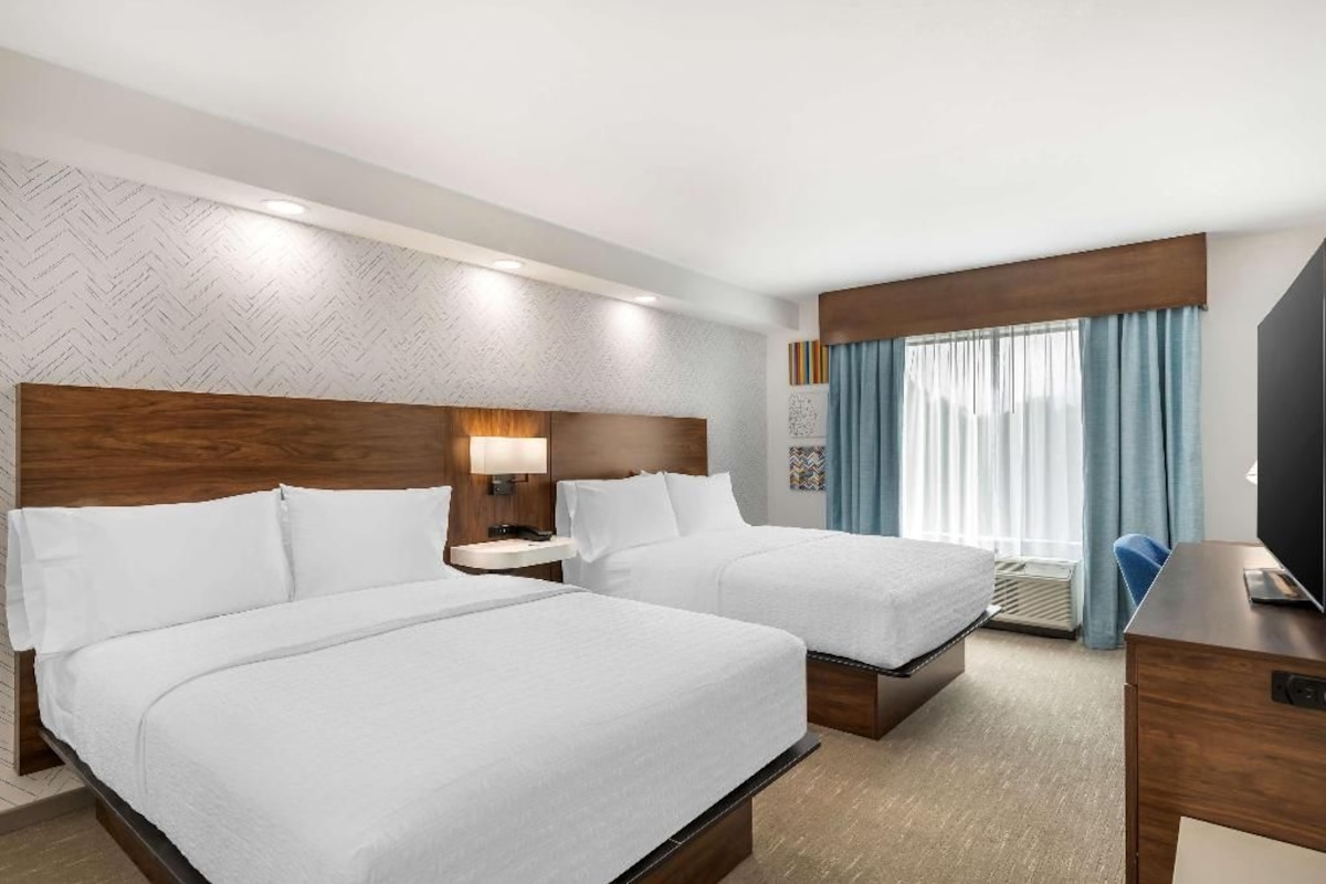 Une chambre d’hôtel avec deux lits, un bureau, une télévision et une fenêtre avec des rideaux.