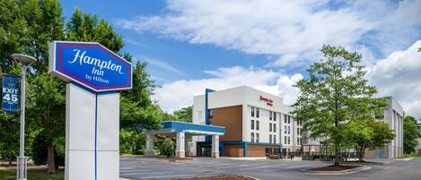 A Hampton Inn by Hilton sign, a parking lot, and a building with a blue and white color scheme.