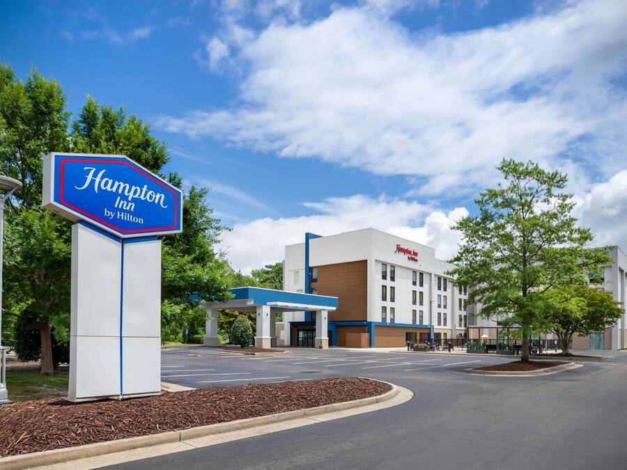 A Hampton Inn by Hilton sign, a parking lot, and a building with a blue and white color scheme.