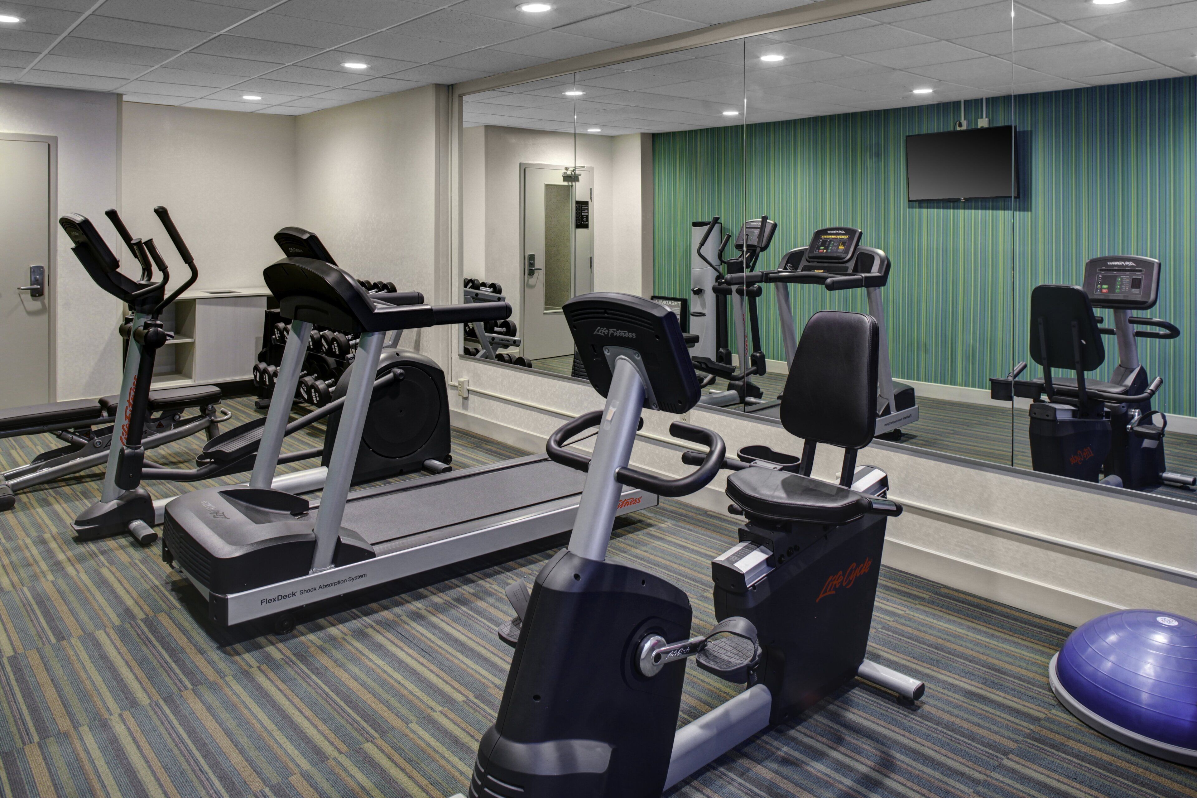 Ett gym med olika typer av träningsutrustning, inklusive löpband, styrketräningsmaskiner och en motionscykel.