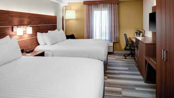 A hotel room with two beds, a desk, a chair, a TV, and a window with curtains.