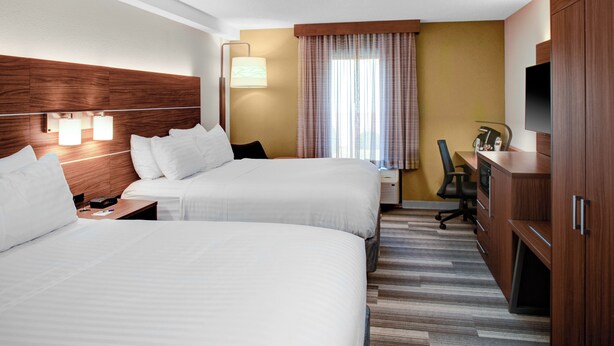 Ein Hotelzimmer mit zwei Betten, einem Schreibtisch, einem Stuhl, einem Fernseher und einem Kleiderschrank.