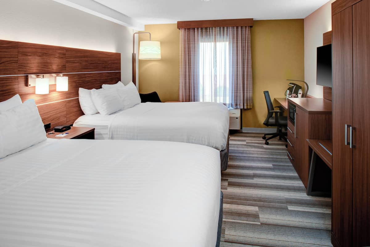 A hotel room with two beds, a desk, a chair, a TV, and a wardrobe.
