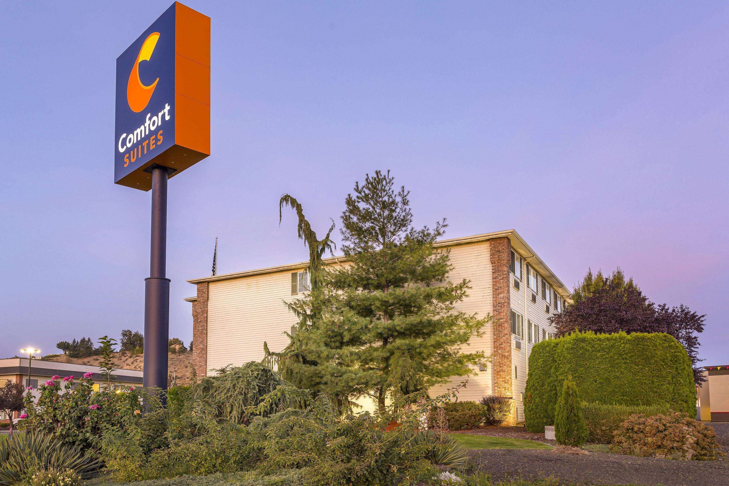 A Comfort Suites hotel with a large sign, surrounded by well-maintained landscaping and a building with a brick facade.