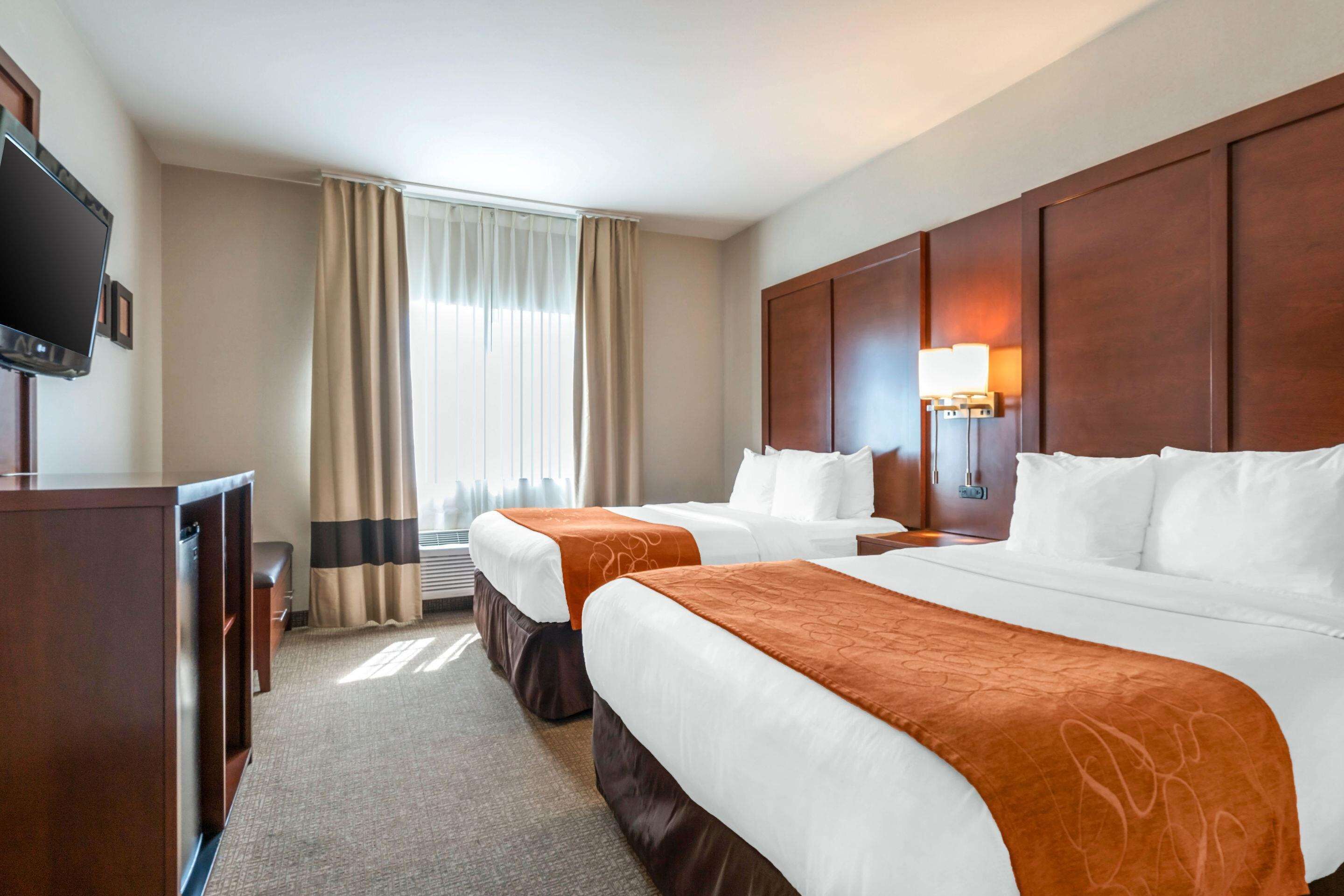 A hotel room with two beds, a TV, a desk, and a window with curtains.