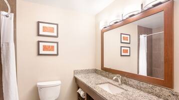 A bathroom with a toilet, sink, and shower. There are framed pictures on the wall.