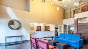 Eine großzügige Lobby mit einem blauen Sofa, roten und schwarzen Sesseln, einem Empfangsbereich und einer Treppe in die obere Etage.
