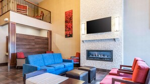 Eine großzügige Lobby mit einem blauen Sofa, roten Sesseln, einem Kamin und einem an einer strukturierten Wand montierten Fernseher.