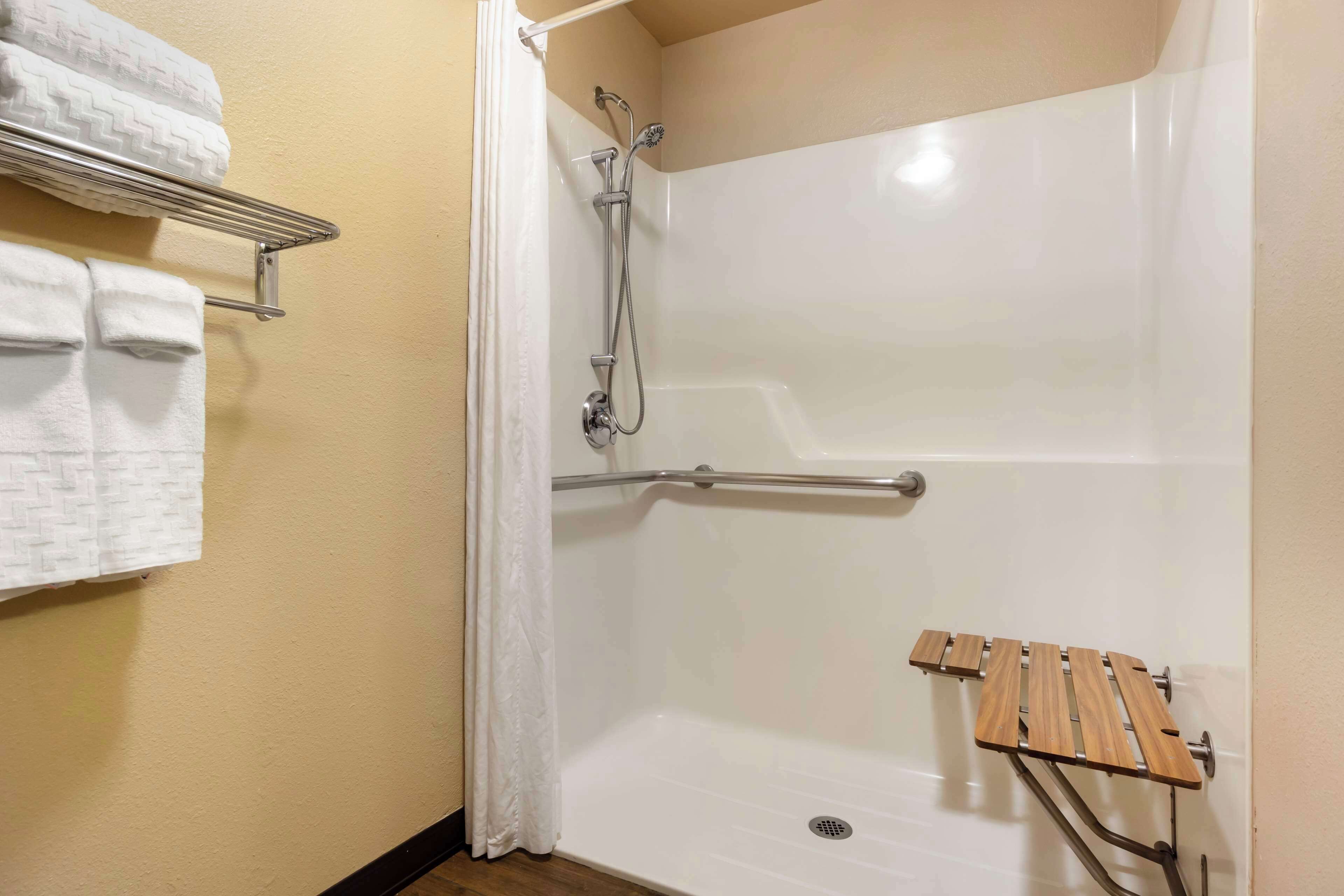 A shower area with a white bathtub, a wooden shelf, and a towel rack with towels.