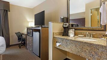 A hotel room with a desk, television, minibar, coffee maker, and a bathroom with a granite countertop and sink.