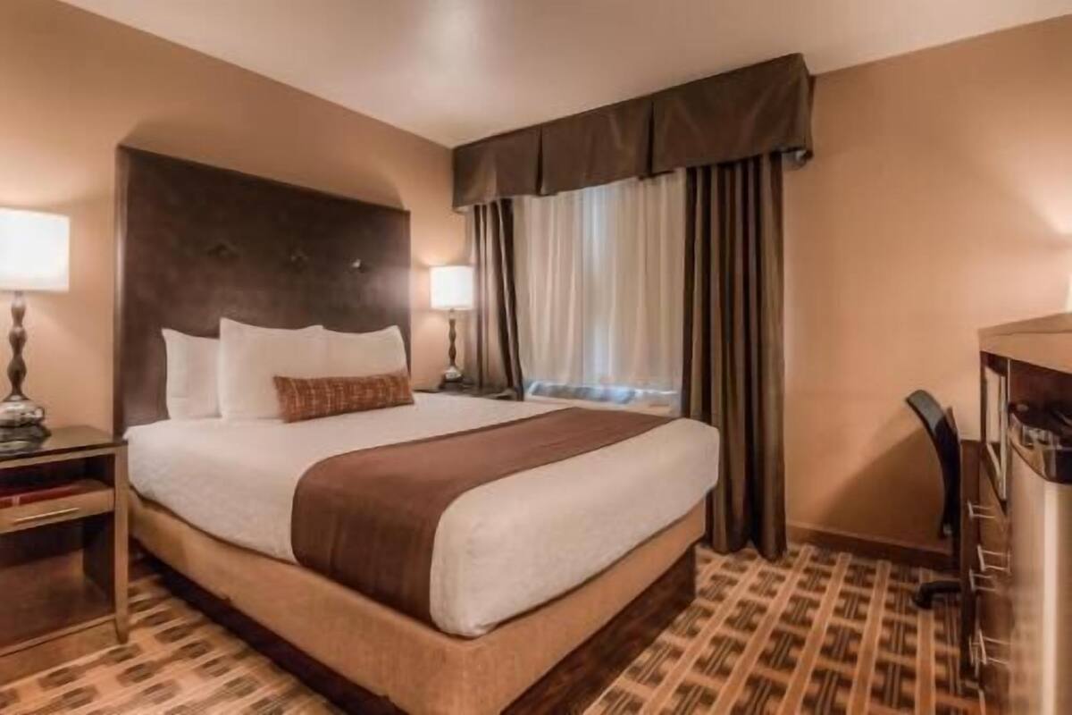 Une chambre d’hôtel avec un grand lit, un bureau, une chaise et une fenêtre avec des rideaux.