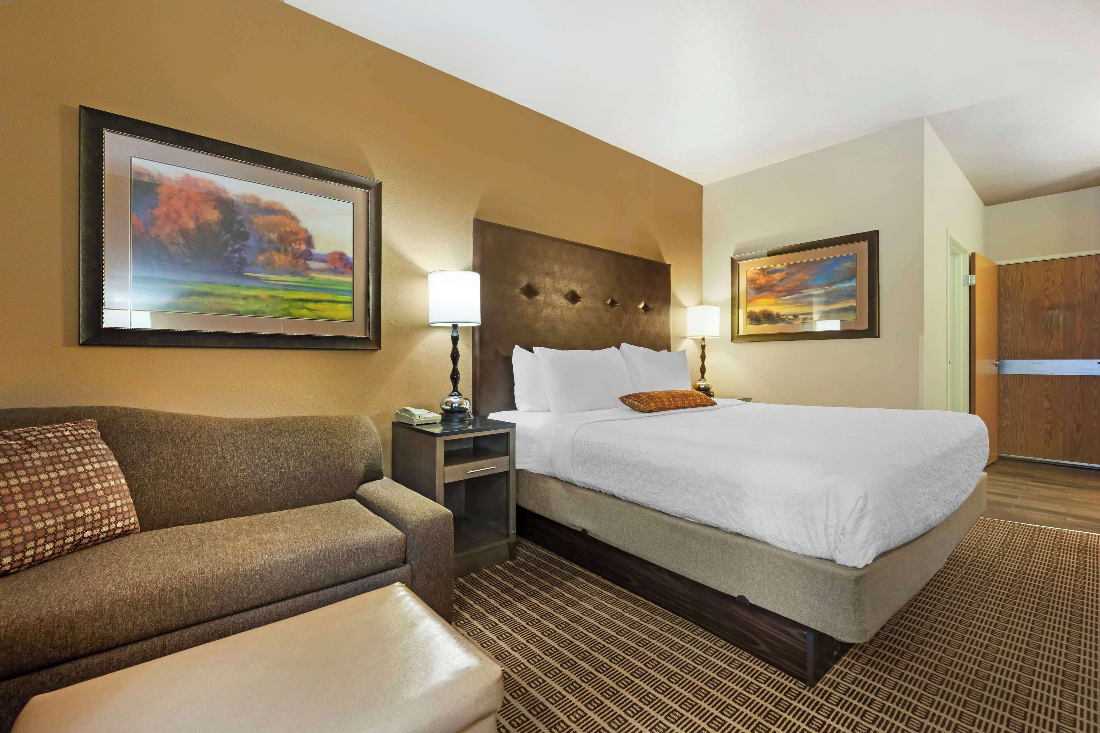A hotel room with a bed, a sofa, a nightstand, and a wall-mounted TV.