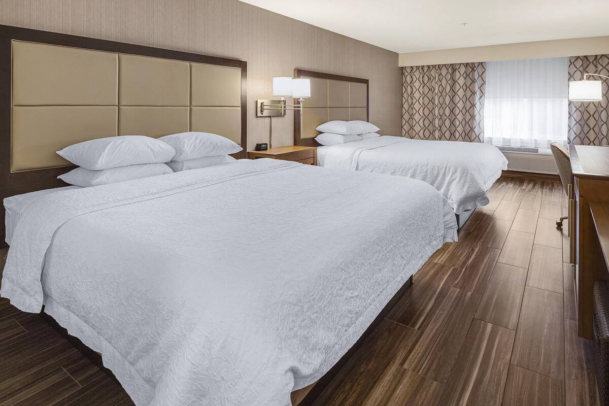 A hotel room with two beds, a desk, and a chair.