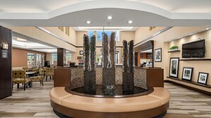 A lobby with a central fountain, seating area, and a TV mounted on the wall. - Hampton Inn & Suites Seattle-North/Lynnwood (Lynnwood)