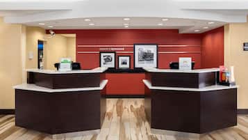Un hall d'accueil d'hôtel avec deux comptoirs de réception, un mur rouge orné d'une enseigne « Bienvenue à Lynnwood », des tableaux encadrés et une enseigne « Hilton Honors ».
