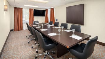 A conference room with a long table, six chairs, and a flat-screen TV on the wall.