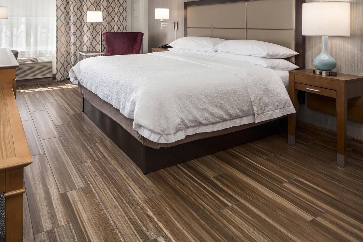 A hotel room with a large bed, a red chair, a bedside table with a lamp, and a patterned wall.